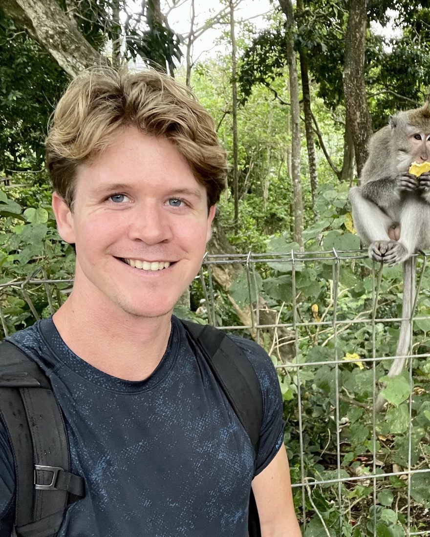 Brandon smiling in a forest beside a monkey