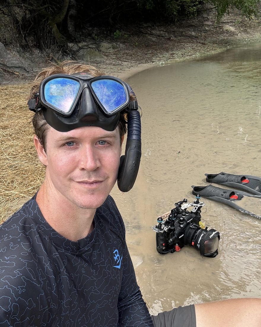 Brandon in a dive mask beside his underwater camera