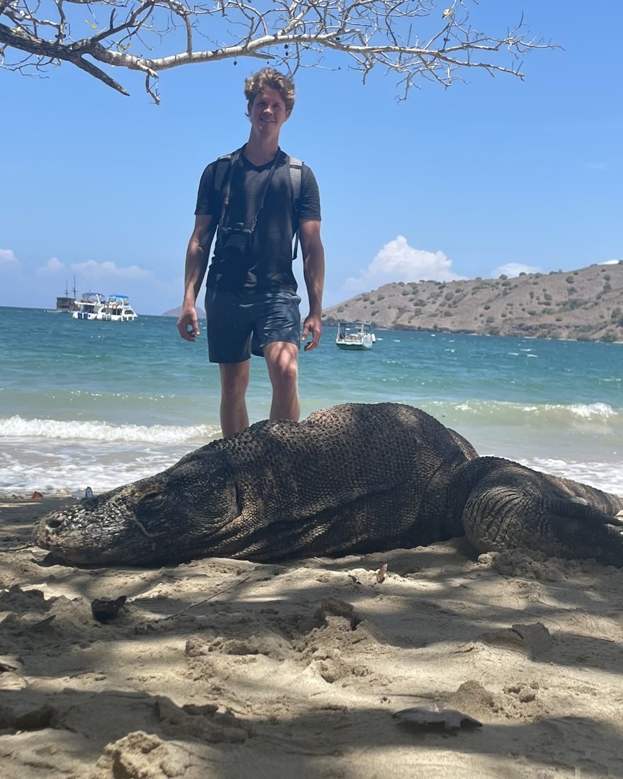 Brandon on a beach behind a resting Komodo dragon